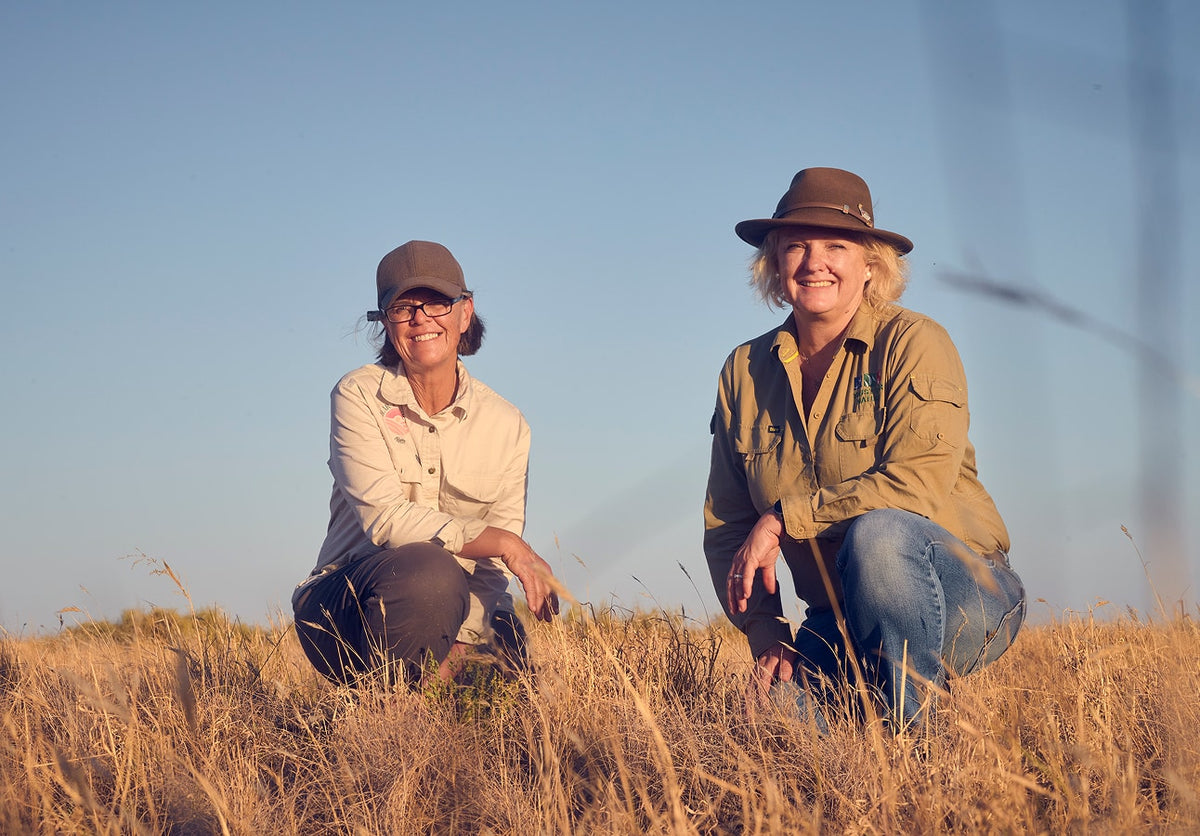 Jo Bear and a Trust for Nature representative crouching in native grassland